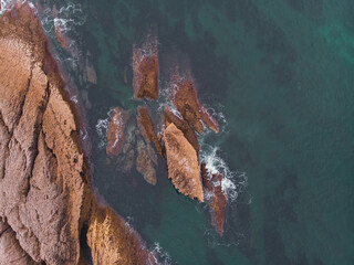 Aerial top view of sea waves hitting rocks on the beach with turquoise sea water.