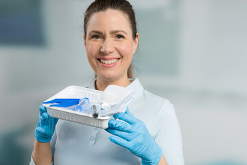 A smiling nurse with a catheter set in front of a clinic room