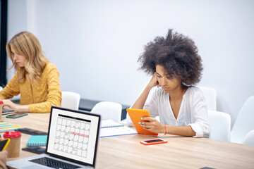 Two girls sitting at the tables in the office and looking busy