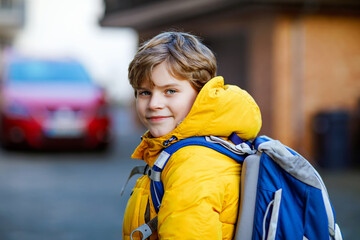 Little school kid boy of elementary class walking to school. Portrait of happy child on the street with traffic. Student with in yellow jacket and backpack in colorful winter clothes.