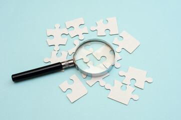 Magnifying glass over white puzzle on blue background