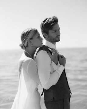 A just married couple standing on a beach, enjoying their time and the bride holding her groom's back
