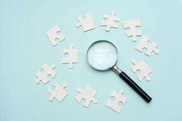 Magnifying glass and white puzzle on blue background