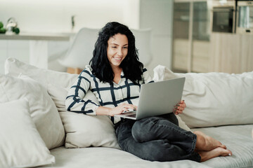 A brunette woman works at home on a laptop computer. Does an online learning task. Modern apartment.