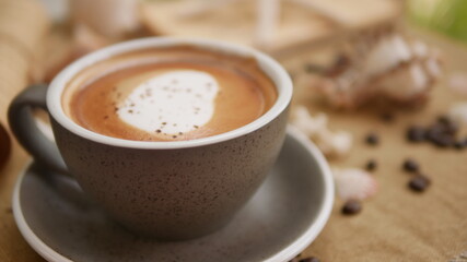 A cup of cappuccino with shell-shaped and coffee bean background.