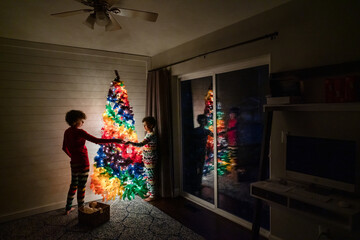 Siblings decorate rainbow tree in dining room