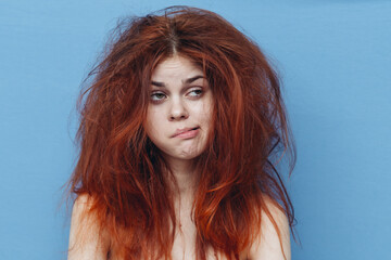 upset red-haired woman with tousled hair on blue background gesturing with her hands