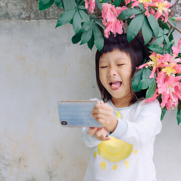 Naklejki Little girl using mobile phone outdoors under pink tree