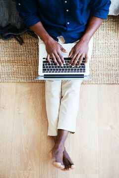 Barefoot black man typing on laptop at home