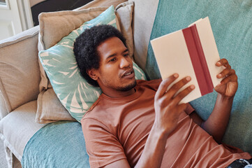Young man reading a book on his sofa