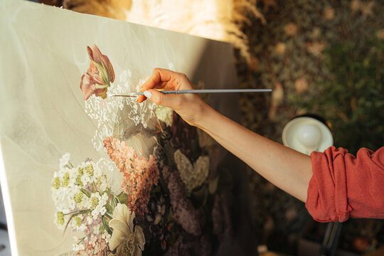 Crop woman painting flowers on canvas