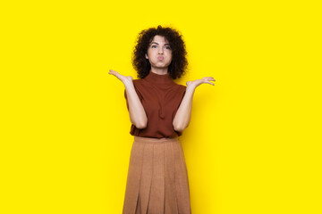 amazing curly haired woman is gesturing with her lips and hands posing in a dress on a yellow studio wall