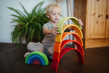 Blond toddler boy playing with open-ended rainbow toy indoors
