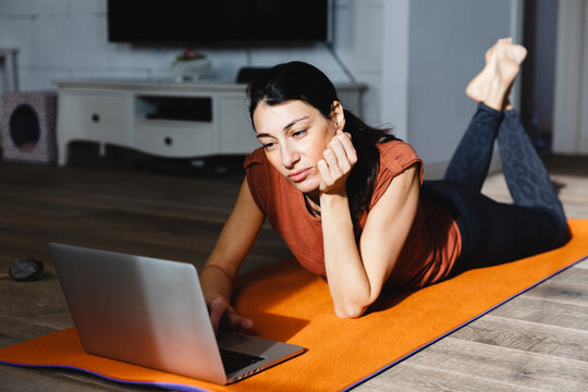 Beautiful woman on yoga mat using laptop at home