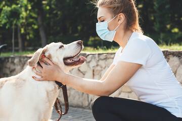 Blonde woman wearing medical mask is playing with her golden retriever during a walk in the park