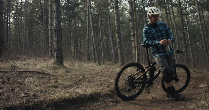 Mountain biker rests on mtb bike drink from flask chill in dark woods