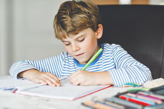 Portrait of cute healthy happy school kid boy at home making homework. Little child writing with colorful pencils, indoors. Elementary school and education. Kid learning writing letters and numbers