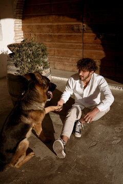Fashionable man playing with his cute dog at home, in the countryside