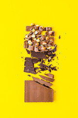 Variation von Schokolade Stücken auf einem gelben Hintergrund. Flat lay, Dessert, Nuss.