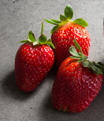 Strawberry close up photo. Three berries on a table. Fruit texture close up. Eating fresh concept. Gray background. 