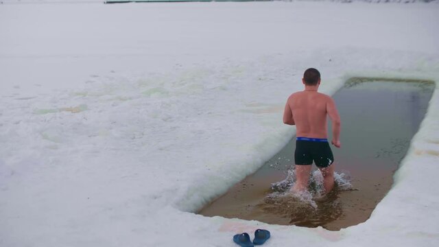 Man bathes in lake covered with ice and snow. Russian traditions