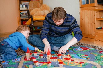 Father and little toddler boy playing with wooden railway, indoors. Happy family, man and cute child moving trains.