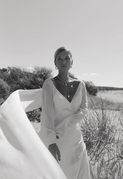 A blonde haired woman standing on the beach wearing a long bridal gown