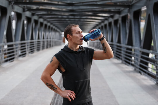 Male athlete drinking water on bridge