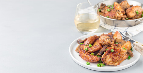 Chicken stew with potatoes, mushrooms and green peas, on a white plate and in metal pot, horizontal, copy space