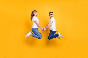 Fototapeta na wymiar Full length photo of funky funny two persons dressed white t-shirt jumping high holding arms isolated yellow color background