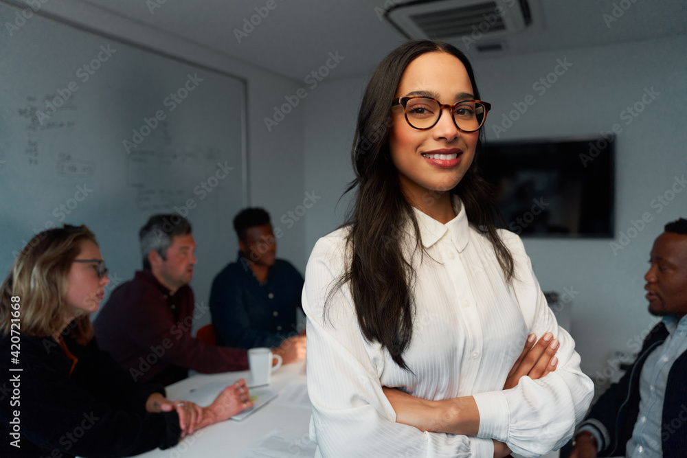 Wall mural confident young female leader smiling and looking at camera with team working at background in offic