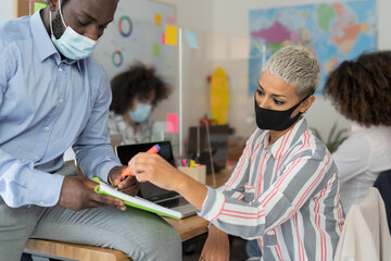 Young people in co-working creative space wearing surgical mask and keeping social distance to avoid corona virus spread - Health care and business technology concept