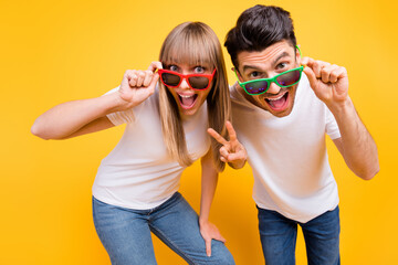 Photo of shiny funky two persons dressed white t-shirt dark glasses showing v-signs isolated yellow color background © deagreez