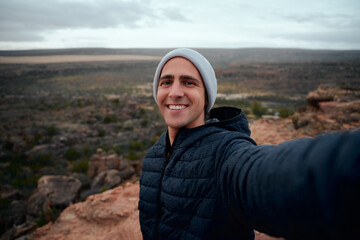 Portrait of happy and smiling hiker taking a selfie on the top of the mountain
