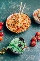 close-up of a dish of chinese noodles with meat and vegetables in plates and chinese chopsticks on a green background