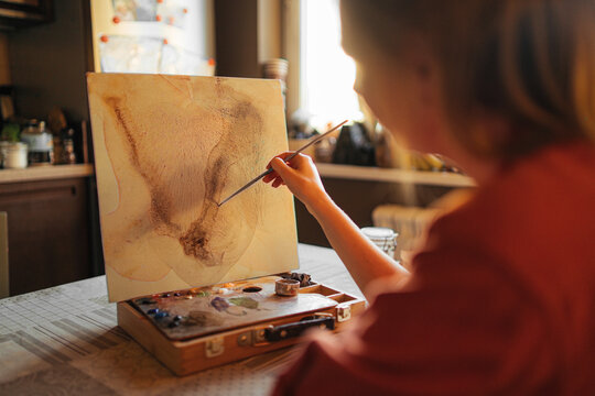 Anonymous woman painting abstract picture in kitchen