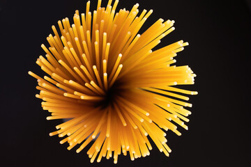 Raw dry spaghetti italian pasta yellow long line it looks like fireworks or flowers bloom on black background with copy space. Concept italian food background.