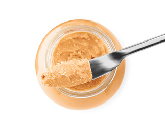 Glass jar and knife with tasty peanut butter on white background, top view