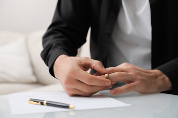 Man taking off wedding ring at table indoors, closeup. Divorce concept
