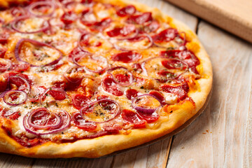 Closeup on hot spicy sausage pizza with onion on the wooden background