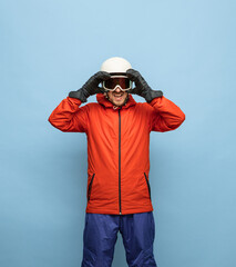 Athletic man in bright ski suit, helmet and goggles isolated on blue background.