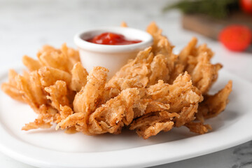 Fried blooming onion with dipping sauce served on white table, closeup