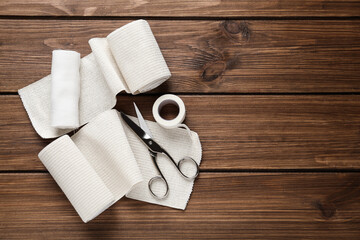 Medical bandage rolls, sticking plaster and scissors on wooden table, flat lay. Space for text