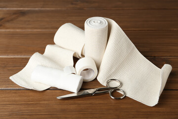 Medical bandage rolls, sticking plaster and scissors on wooden table
