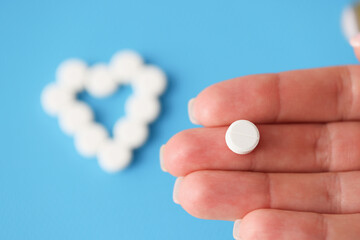 White pill lying on hand on background of heart closeup
