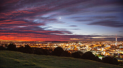Vivid sunset above Auckland city. A moon rises in the center of the frame.