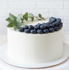 white cake with blueberries and a sprig of eucalyptus. cake with minimalistic decor and copy space
