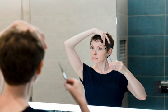 A woman gives herself a haircut at home.