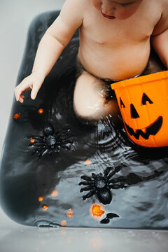 Toddler playing in an halloween bath, catching pompons and spiders