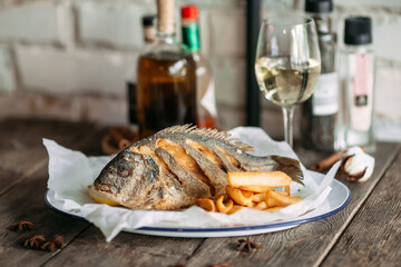 Side view on fried dorado fish with fries chips and white wine